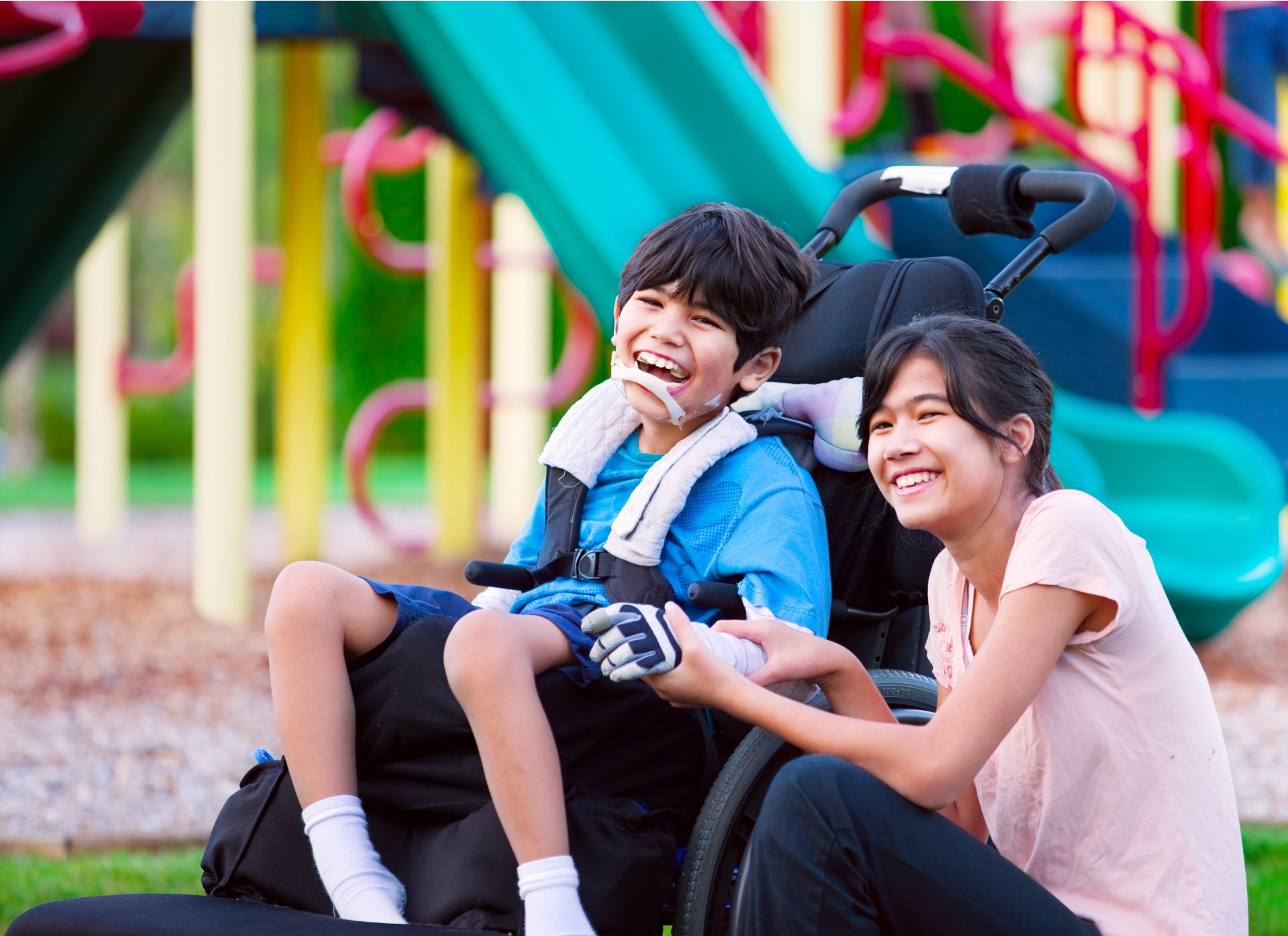 A girl is sitting next to a boy in a wheelchair at a playground.