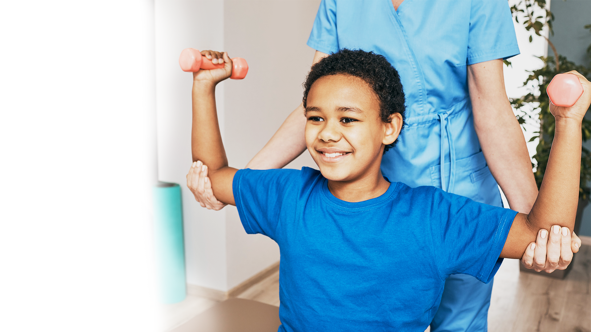 A young boy is lifting dumbbells with a nurse.