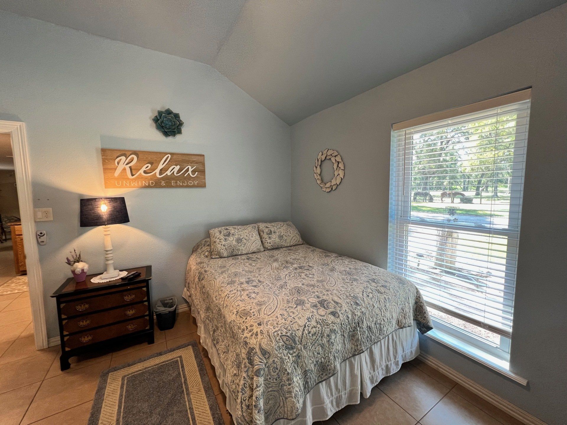 a bedroom with a bed , dresser , lamp and a sign on the wall that says `` relax '' .