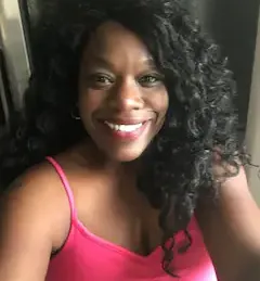 A woman with curly hair is smiling and wearing a pink tank top.