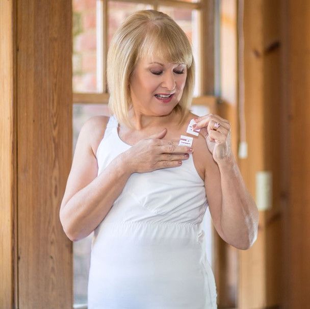 a woman in a white tank top is holding a sticker on her shoulder .