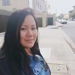 A woman is standing on a sidewalk in front of a building.