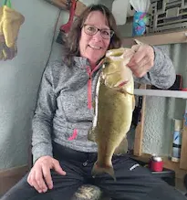A woman is sitting on a bench holding a large fish.