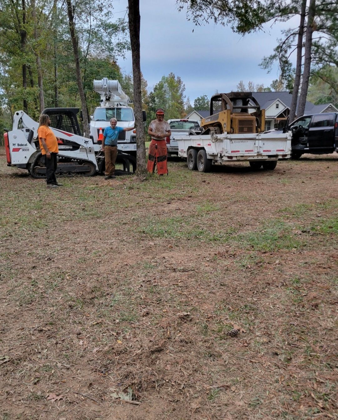 Workers and trucks in a wooded area, with a blue boom lift and white pickup trucks.