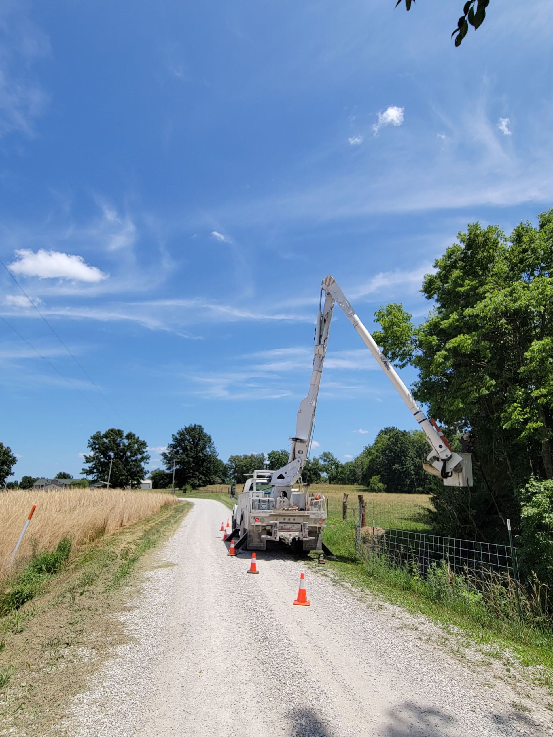 Utility truck with raised boom on a gravel road beside a field under a blue sky