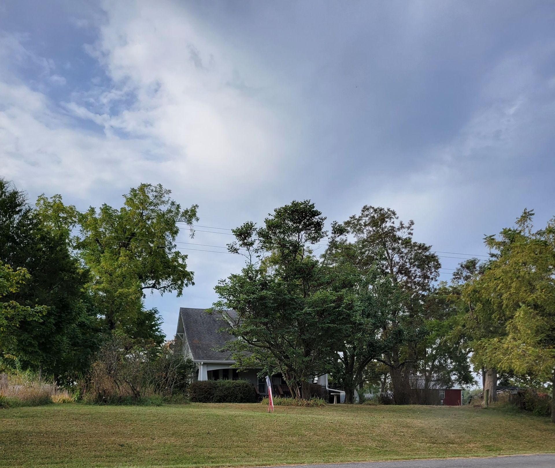 Rural yard with a small house, trees, and a partly cloudy sky