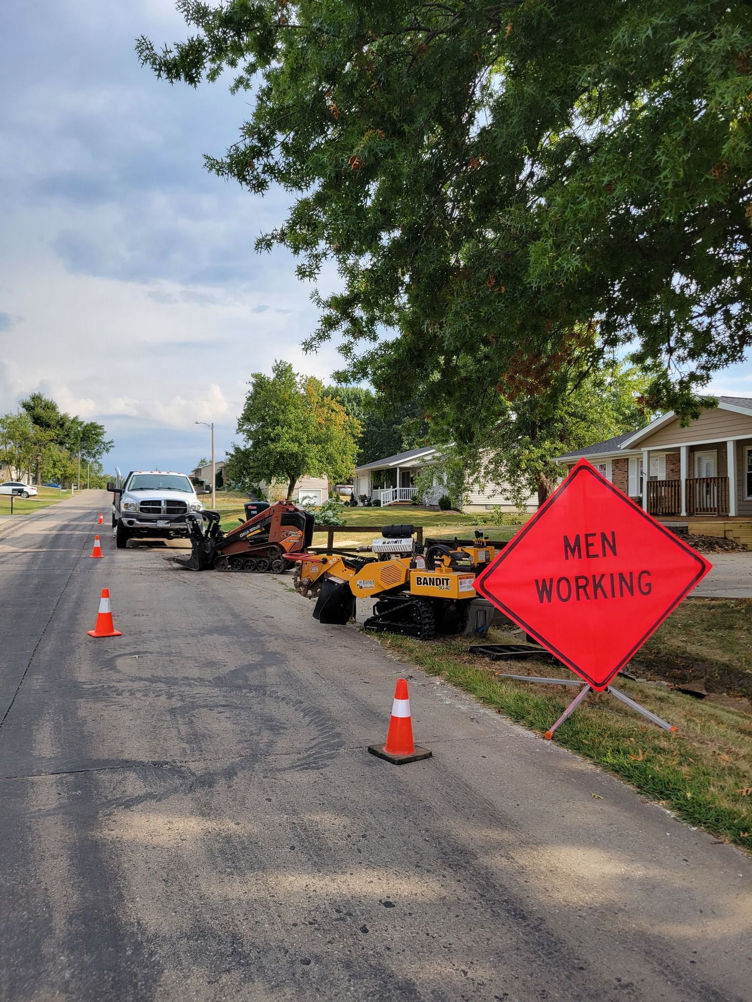 Roadside work zone with orange cones and a red “MEN WORKING” sign along a street.