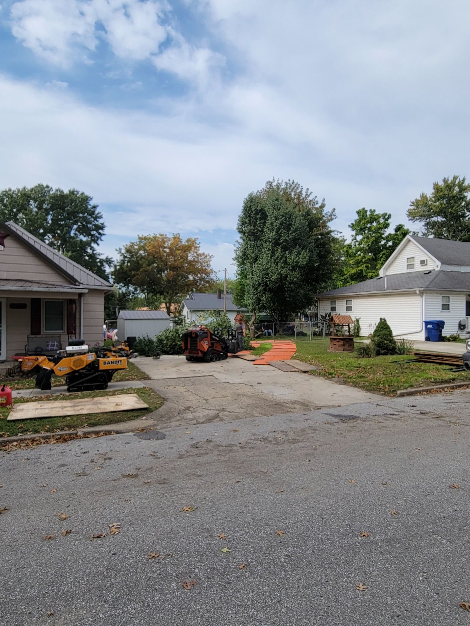 Residential driveway with gravel, potted flowers, and houses on both sides under a cloudy sky