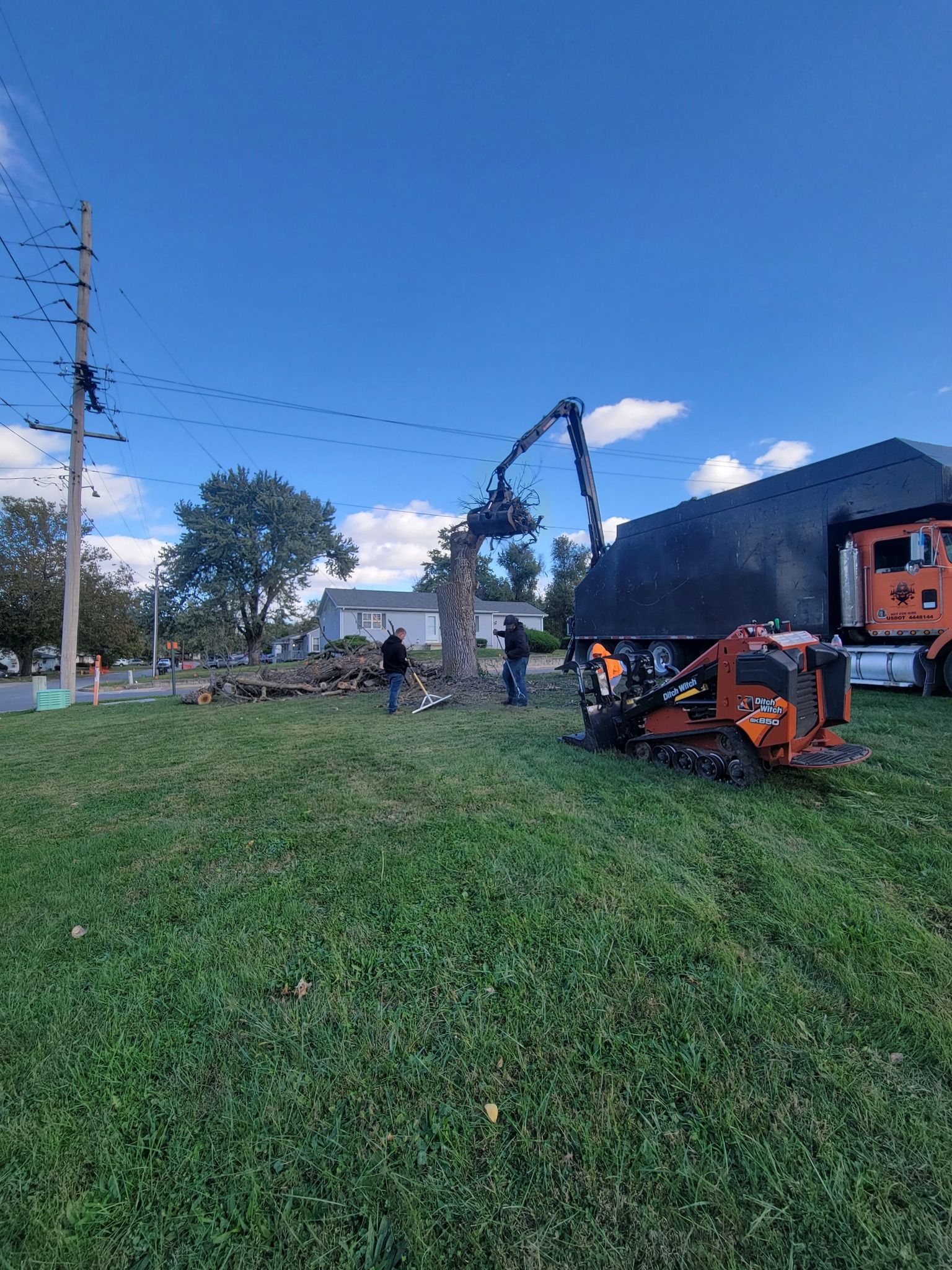Outdoor scene with green grass, utility poles, and orange farm machinery beside a small building under a blue sky.