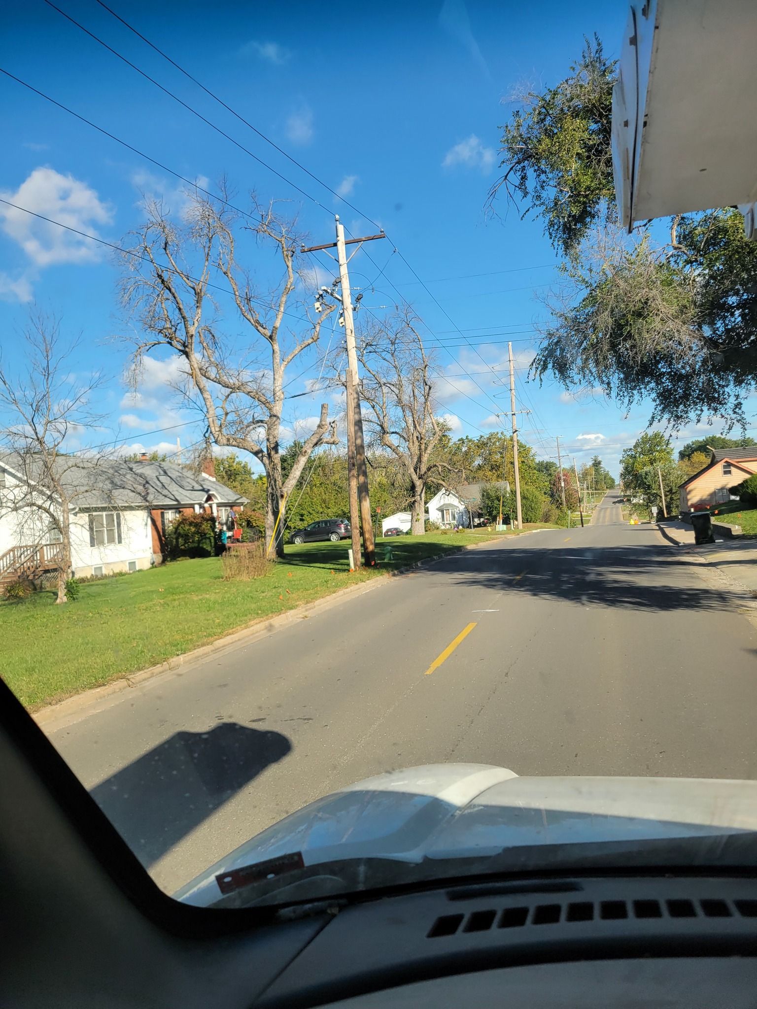 Residential street seen from a car, with leafless trees, houses, and a clear blue sky.