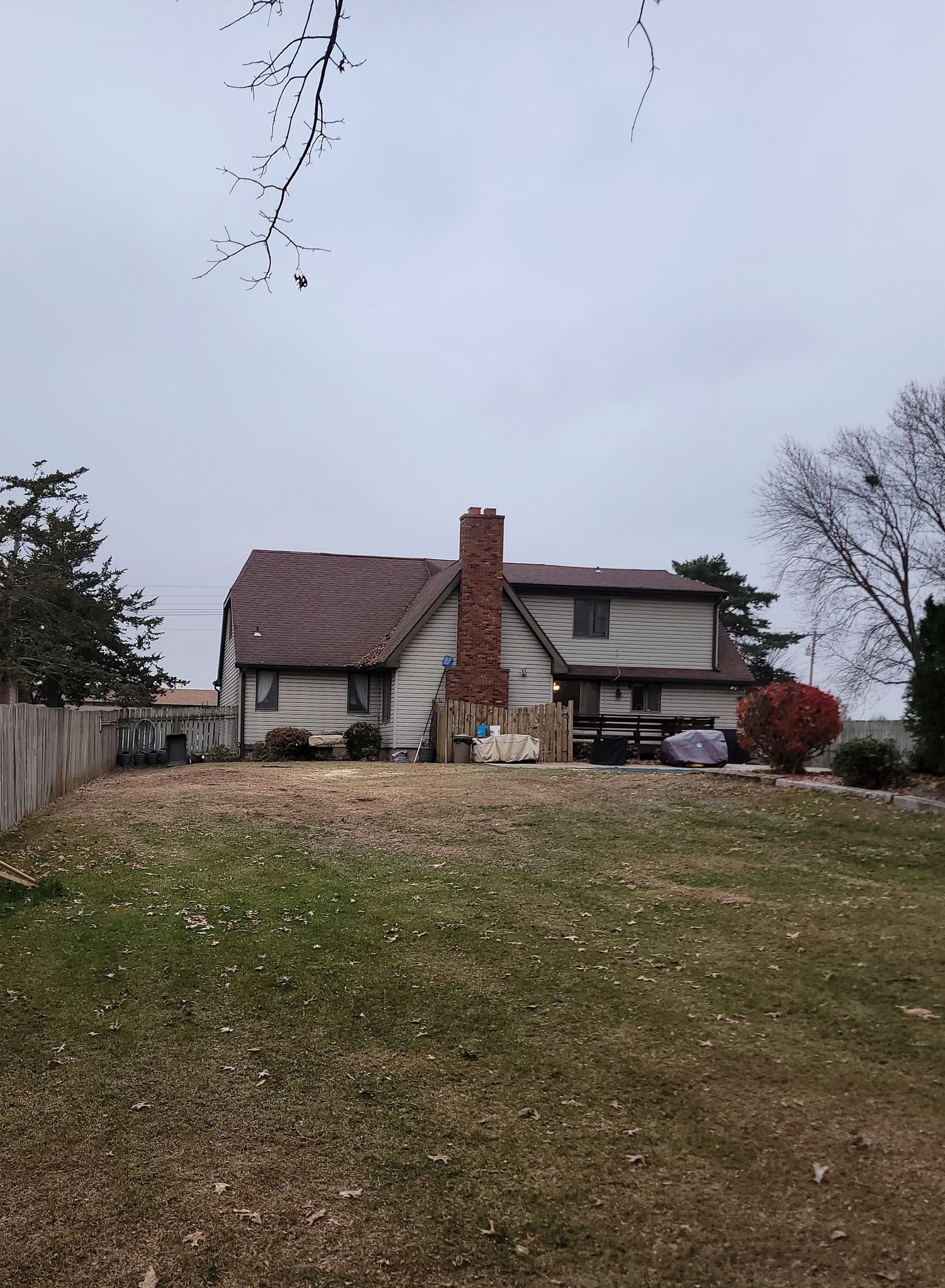 House on a grassy hill under an overcast sky, with a brick chimney and leafless trees nearby