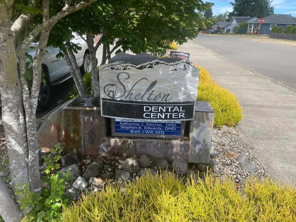 A sign for the shelter dental center is sitting under a tree.