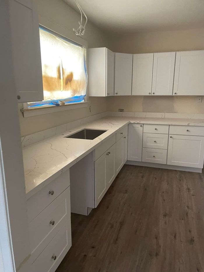 A kitchen with white cabinets , a sink , and a window.