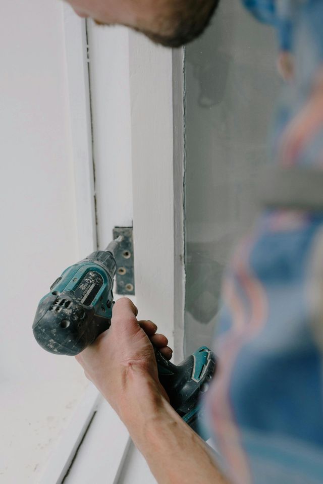 Person using a green cordless drill to install a hinge on a white door frame