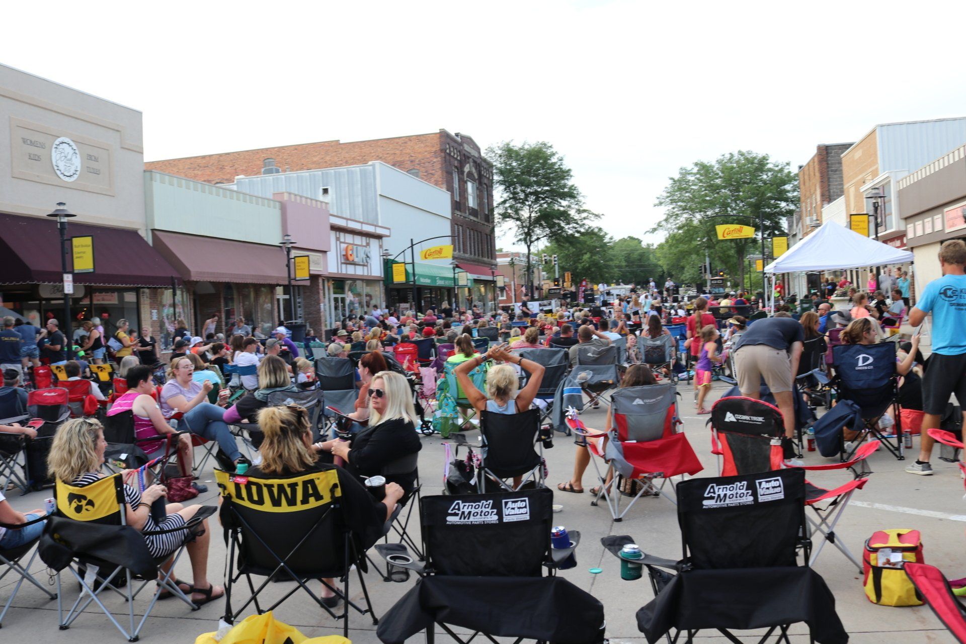 A crowd of people are sitting in chairs on a city street watching a concert.