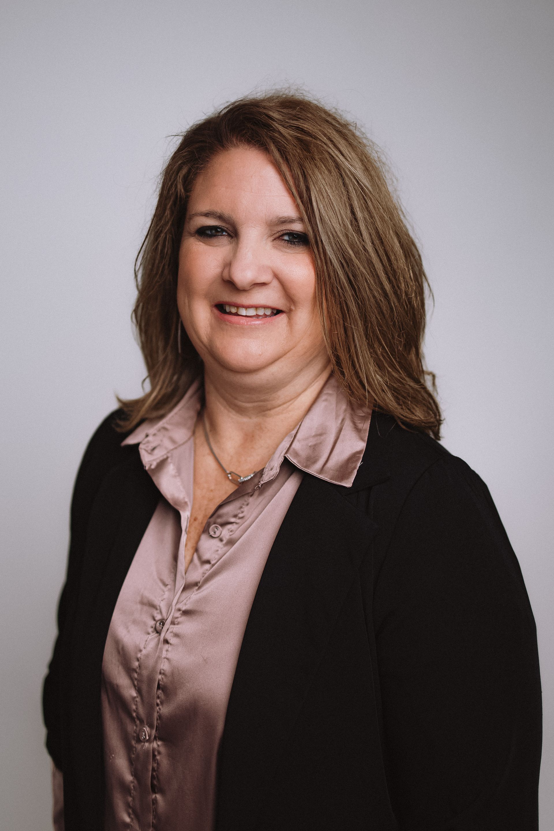 A woman wearing a black jacket and a pink shirt is smiling for the camera.