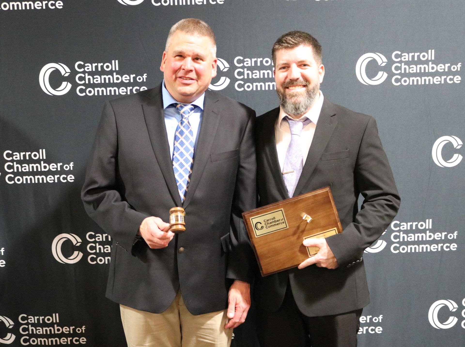 Two men in suits are standing next to each other holding a plaque.