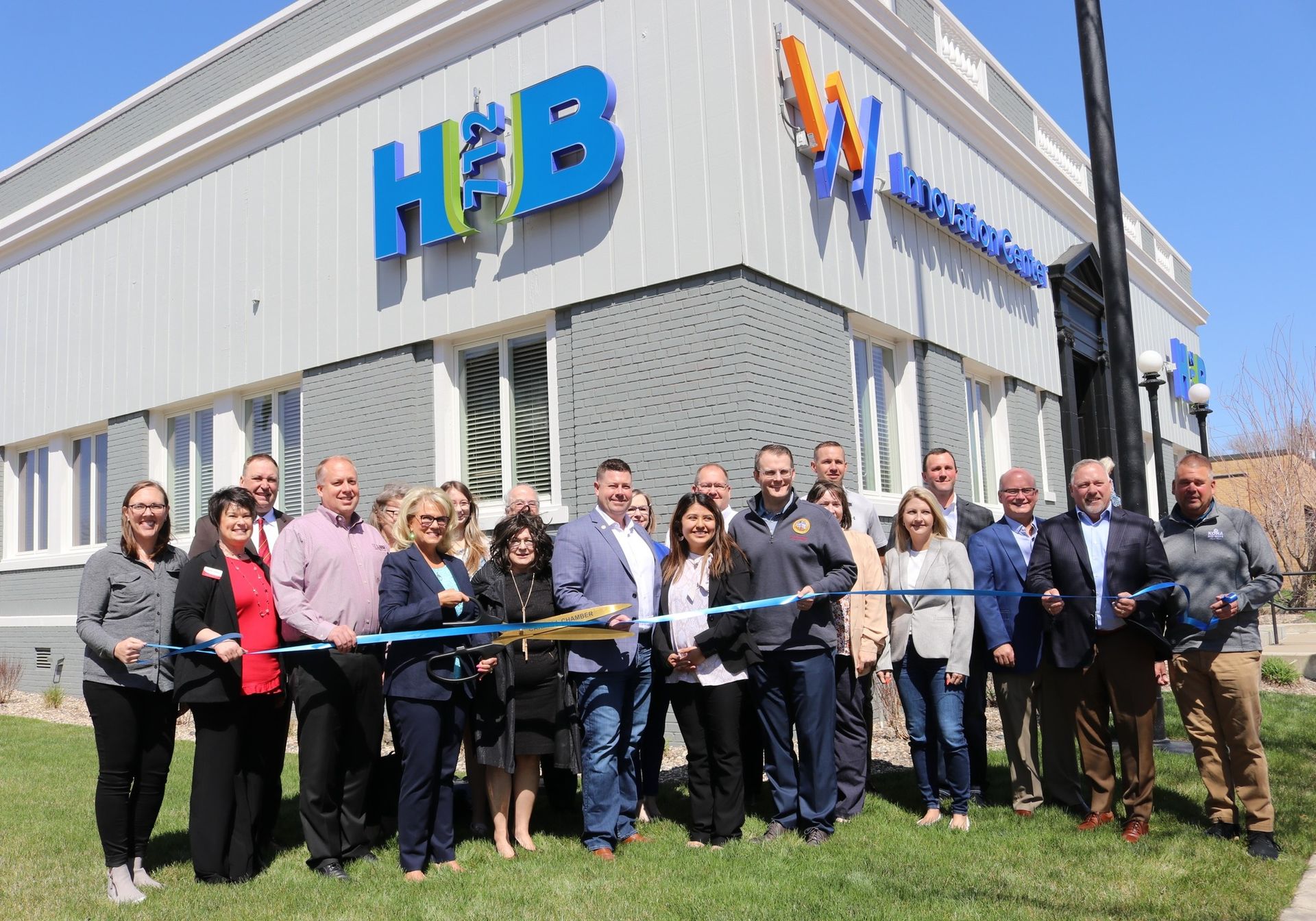 A group of people are cutting a ribbon in front of a building.