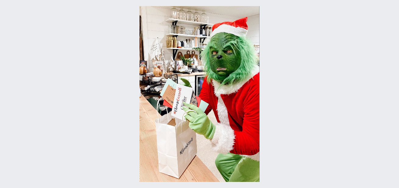 A person dressed as the grinch is holding a gift bag.