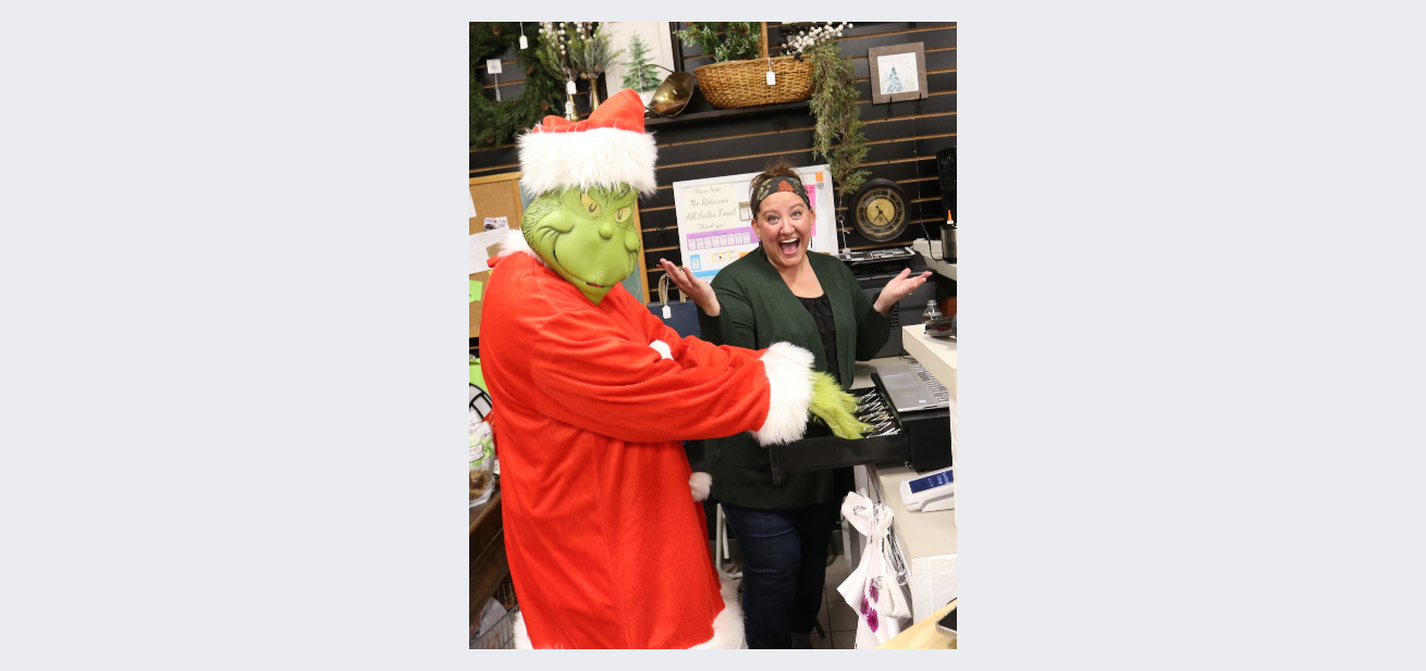 A woman is standing next to a grinch dressed as santa claus.
