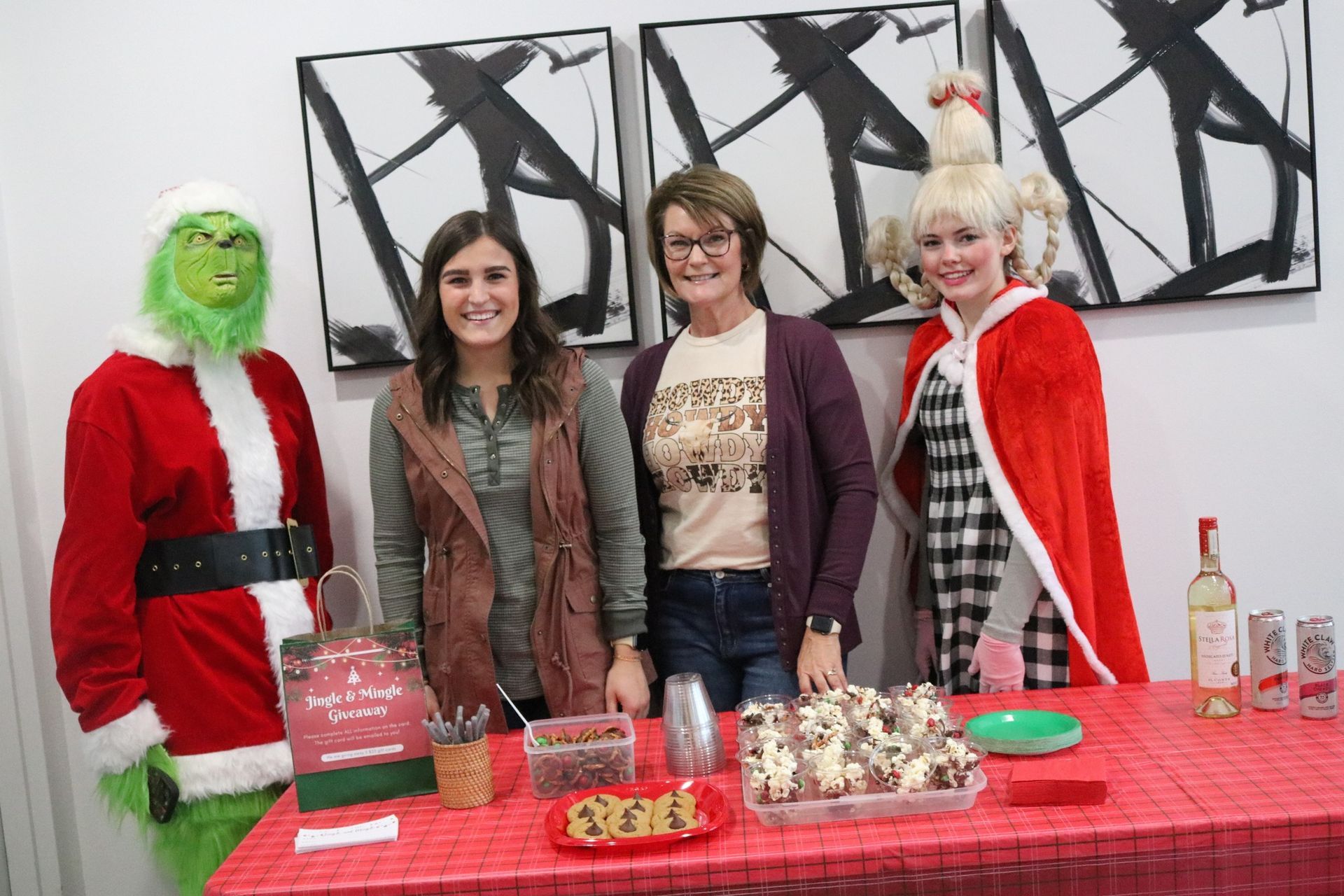 Three women are posing for a picture in front of a table with a grinch costume.