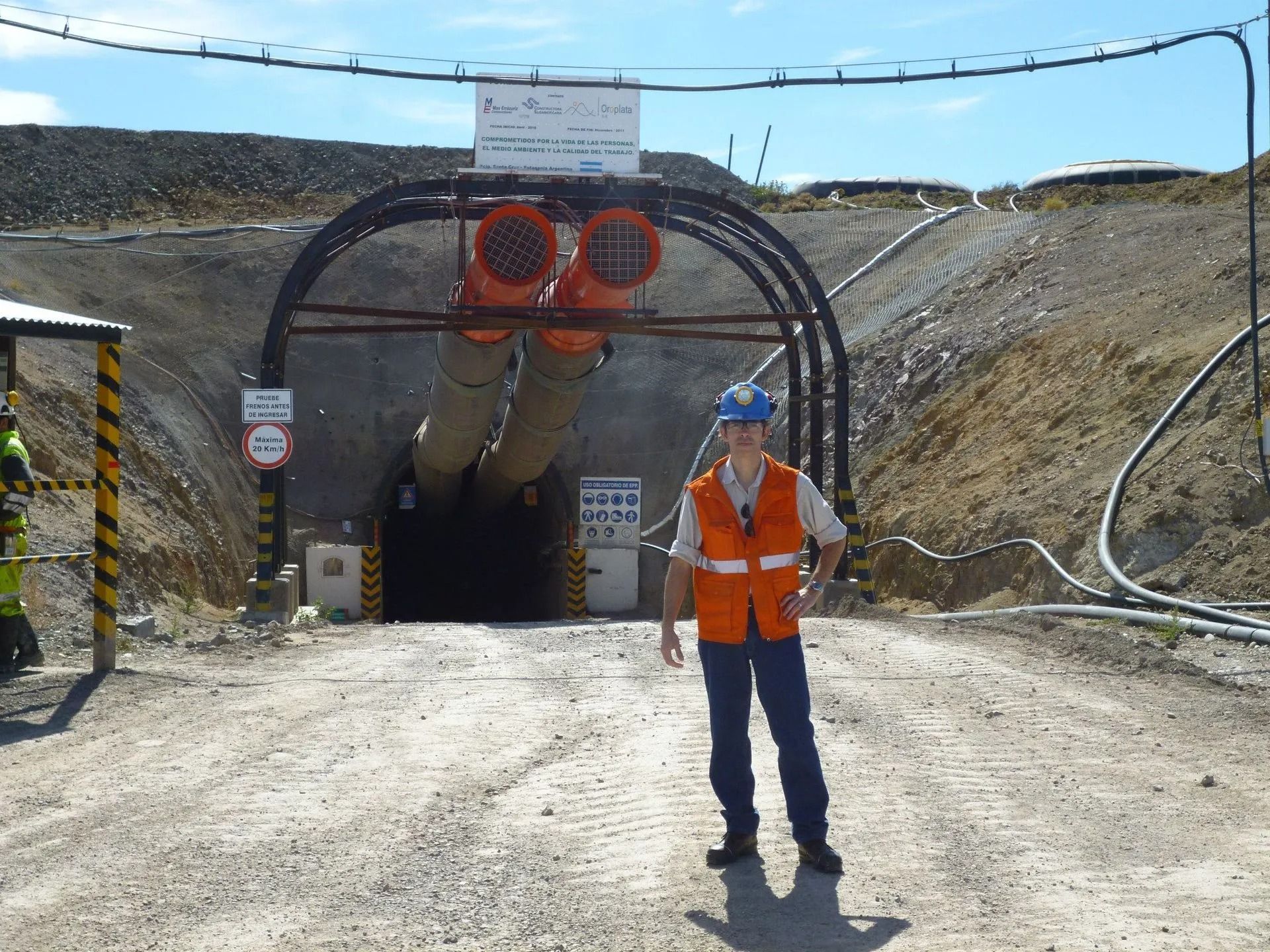 Un trabajador con equipo de seguridad naranja permanece de pie frente a la entrada de un túnel en una obra en construcción.