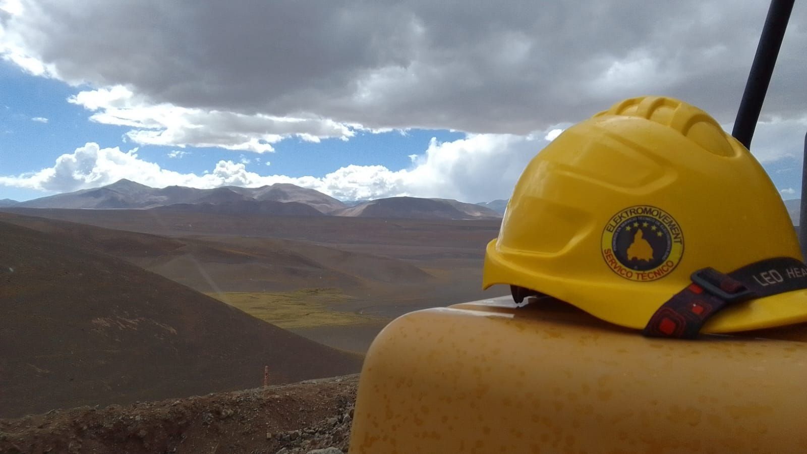 Casco amarillo sobre una cornisa con vistas a un vasto valle rocoso de montaña bajo un cielo nublado.