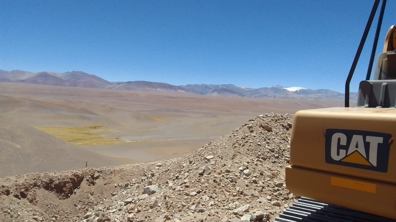 Una excavadora CAT en una ladera rocosa con vistas a un vasto valle desértico y montañas distantes.