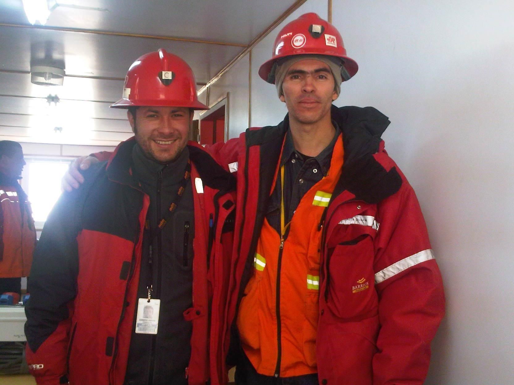 Dos bomberos con uniforme rojo y cascos están de pie en un estrecho pasillo interior.