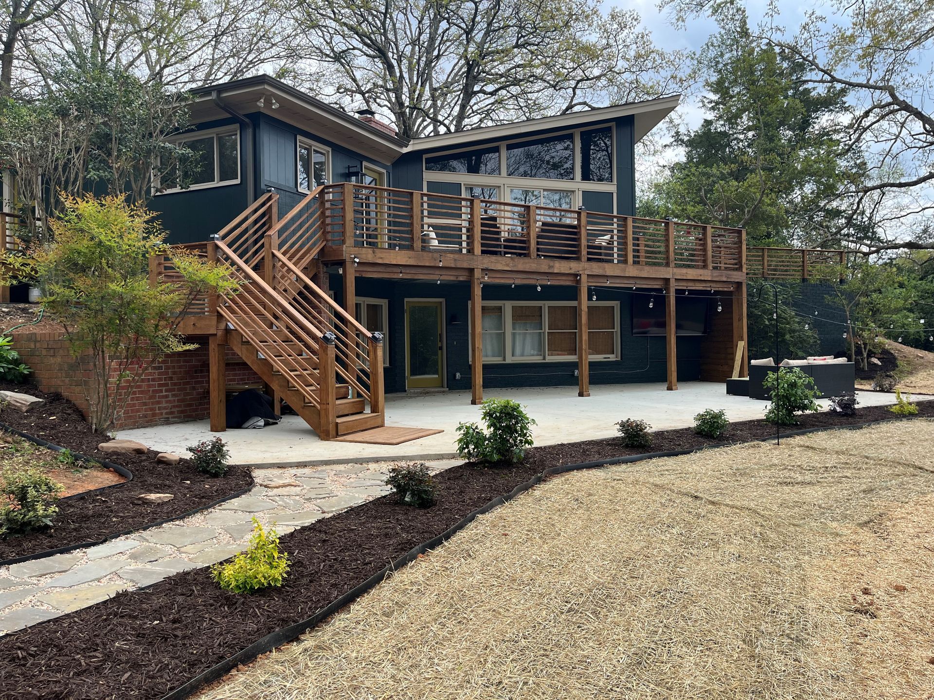 Modern house with wood deck and stairs, set on a landscaped yard with gravel and mulch beds