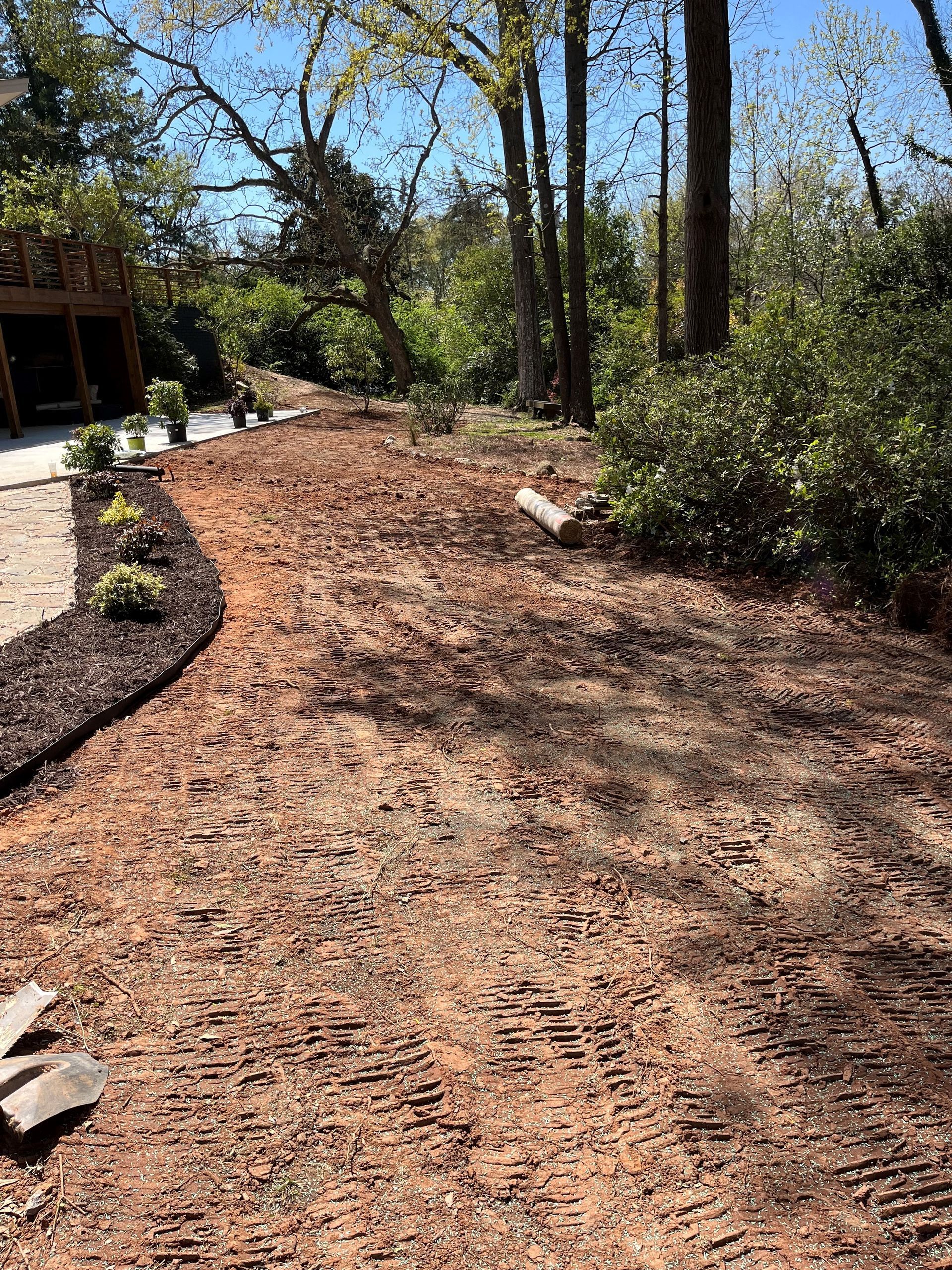 Woodchip garden path beside shrubs and trees, with a stone walkway and building edge on the left.