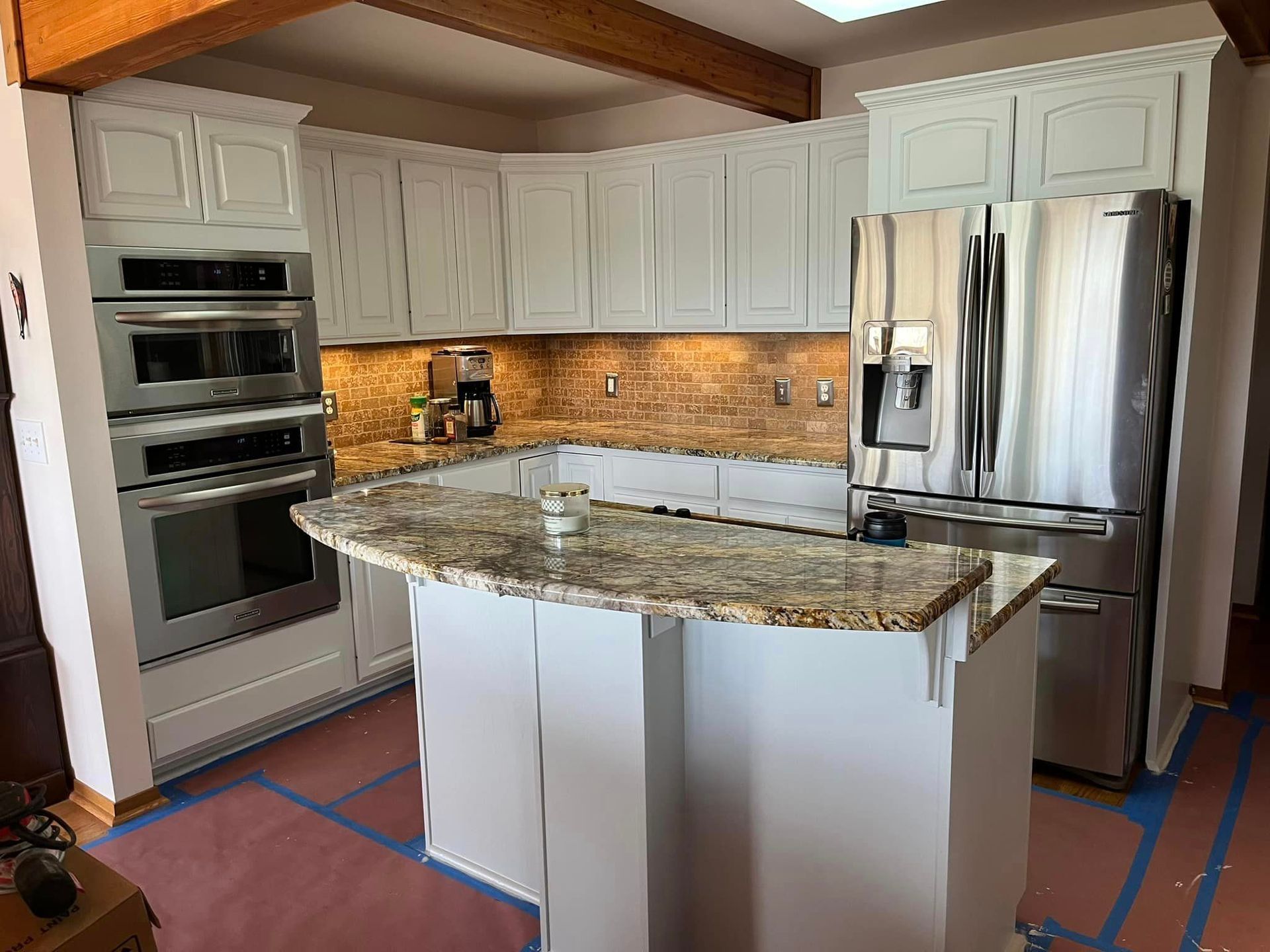 Modern kitchen with white cabinets, granite island, stainless steel appliances, and warm under-cabinet lighting