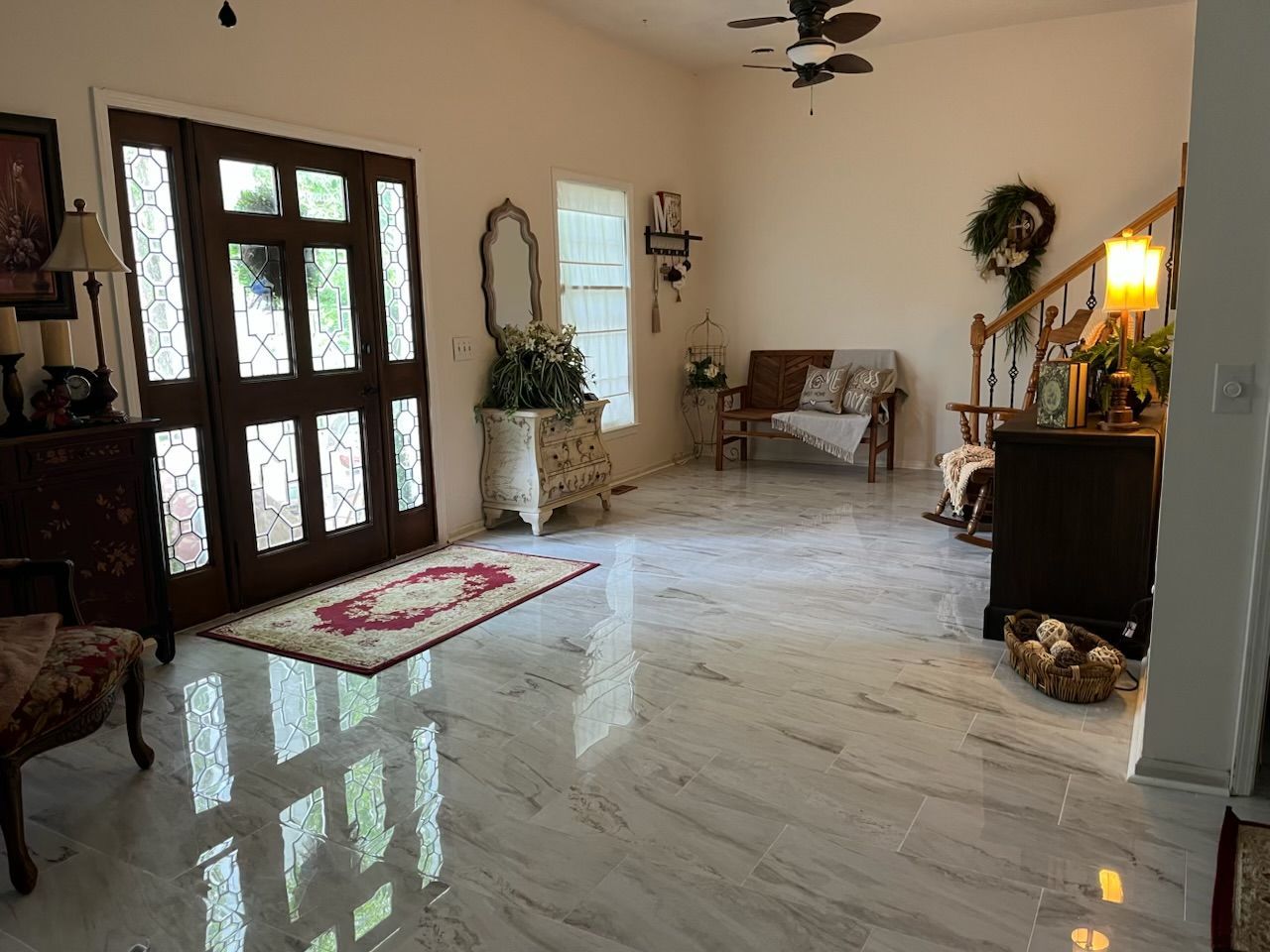 Bright living room with white marble floor, dark wood doors, couch, and decorative plants.