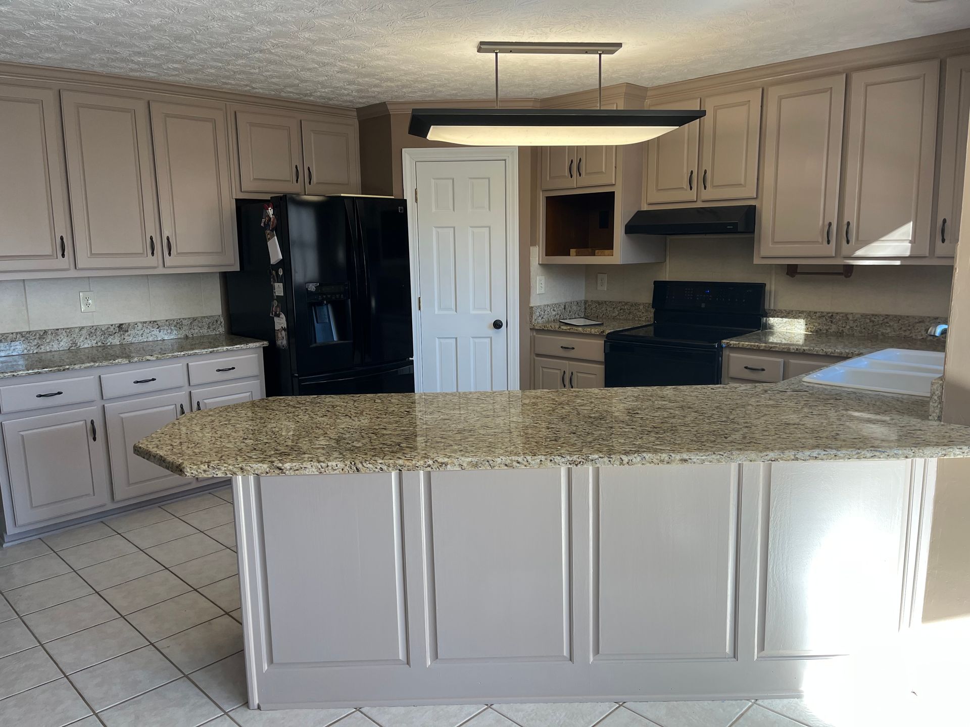 Kitchen with white cabinets, black appliances, and a granite island countertop.