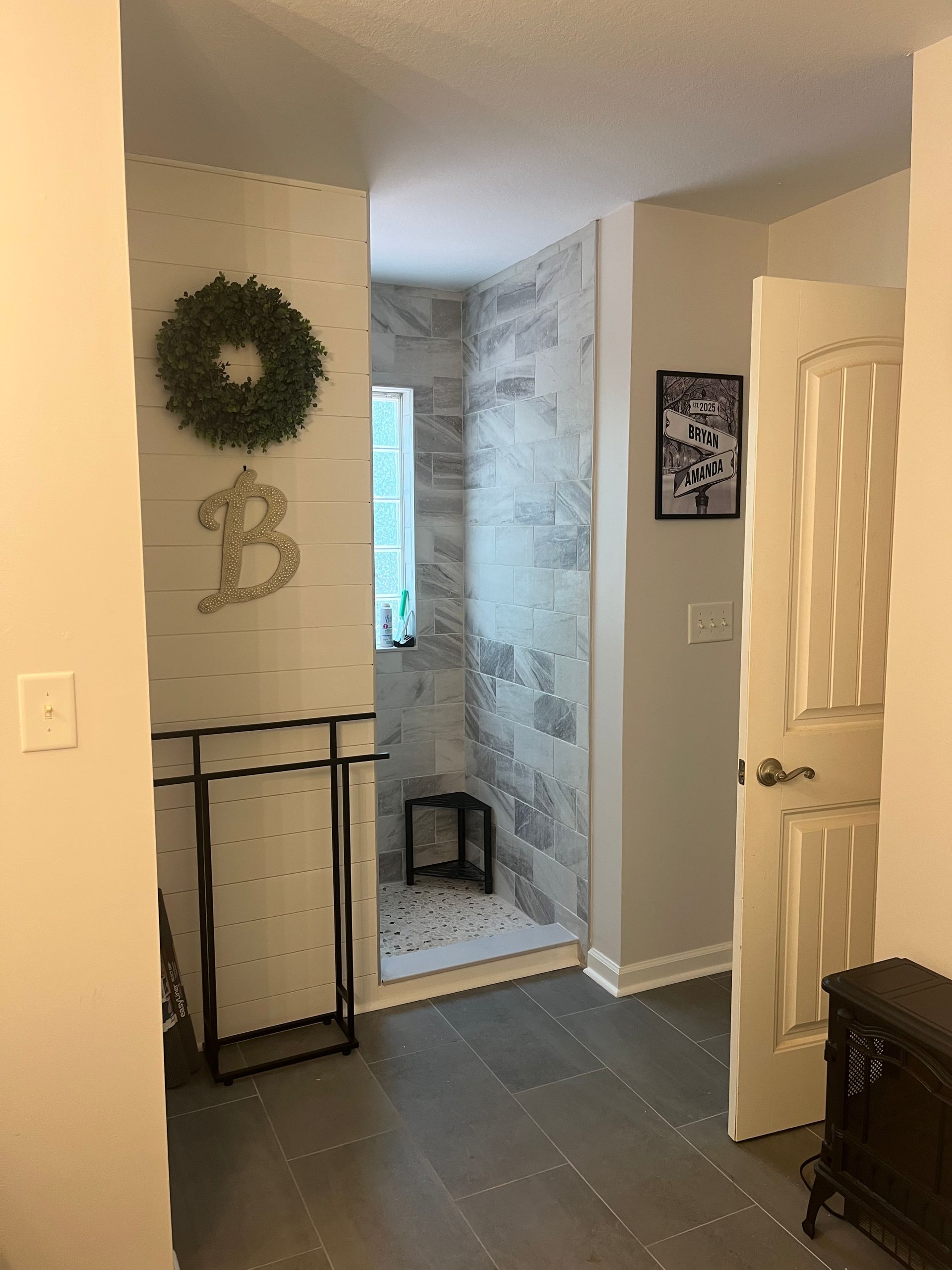 Interior hallway with open bathroom door, gray tile shower, and wreath on the wall