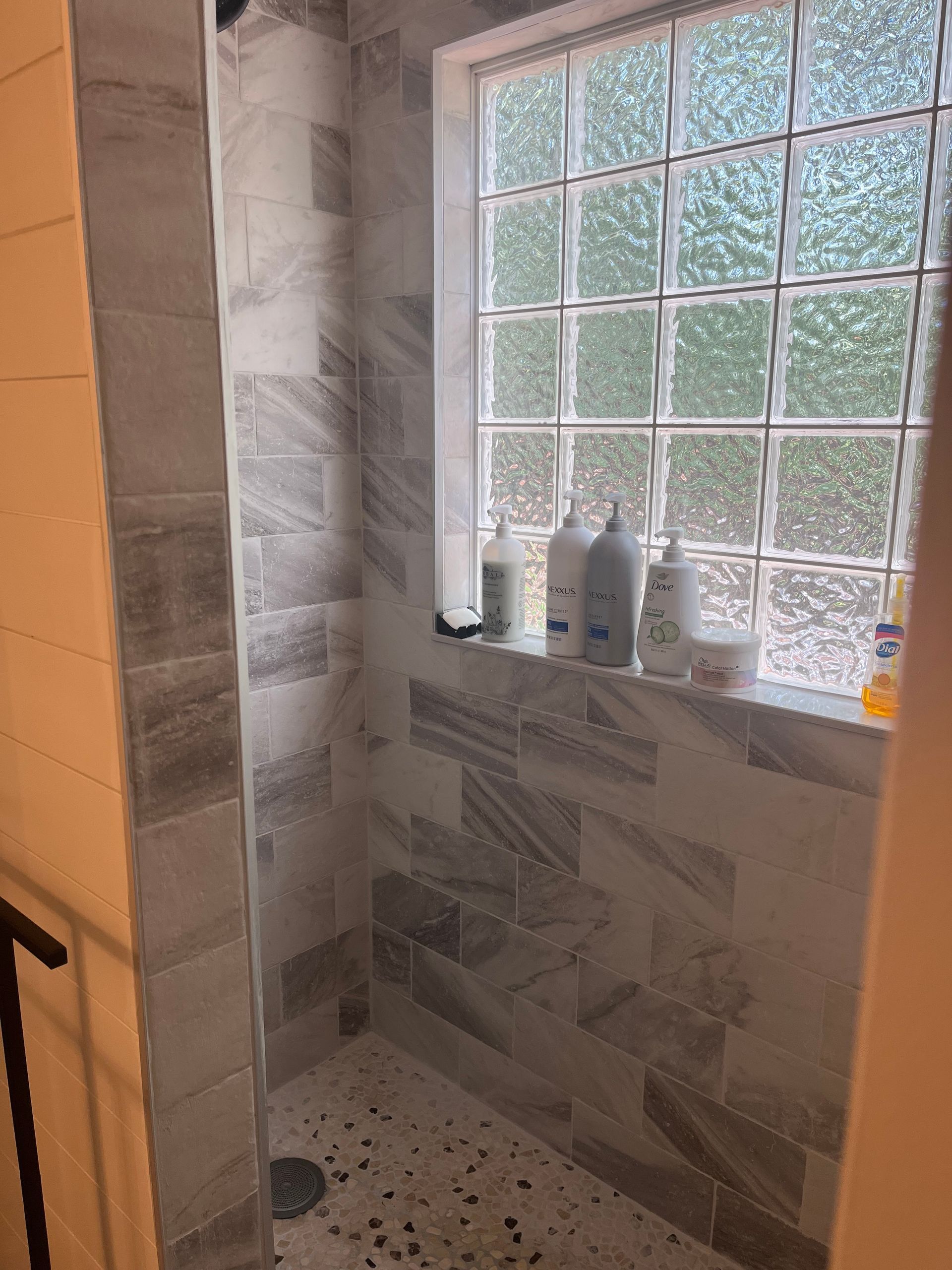 Bathroom shower nook with tiled walls, glass-block window, and bottles on the windowsill.