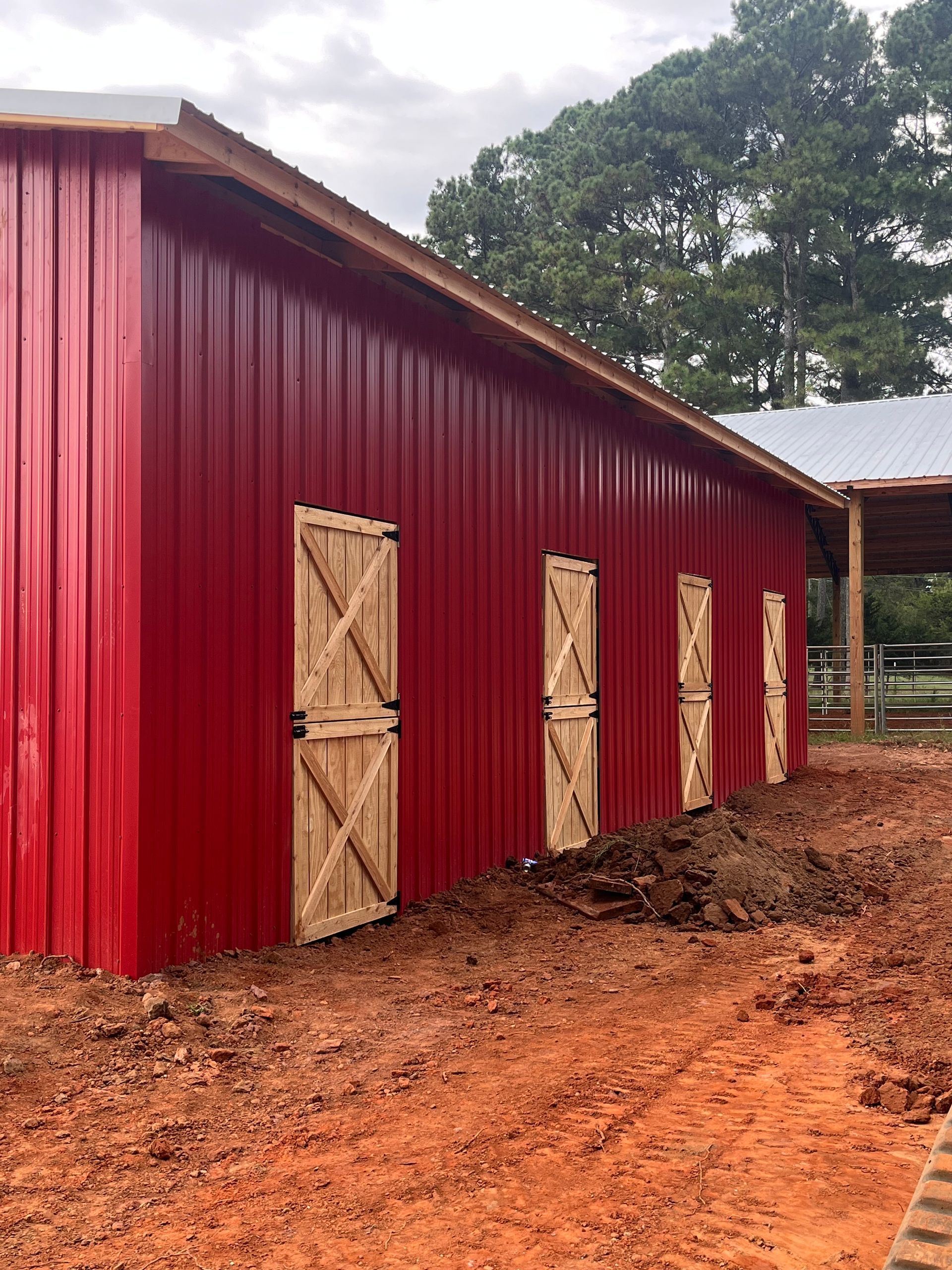 Red metal barn with wooden doors on a muddy dirt path in a rural setting