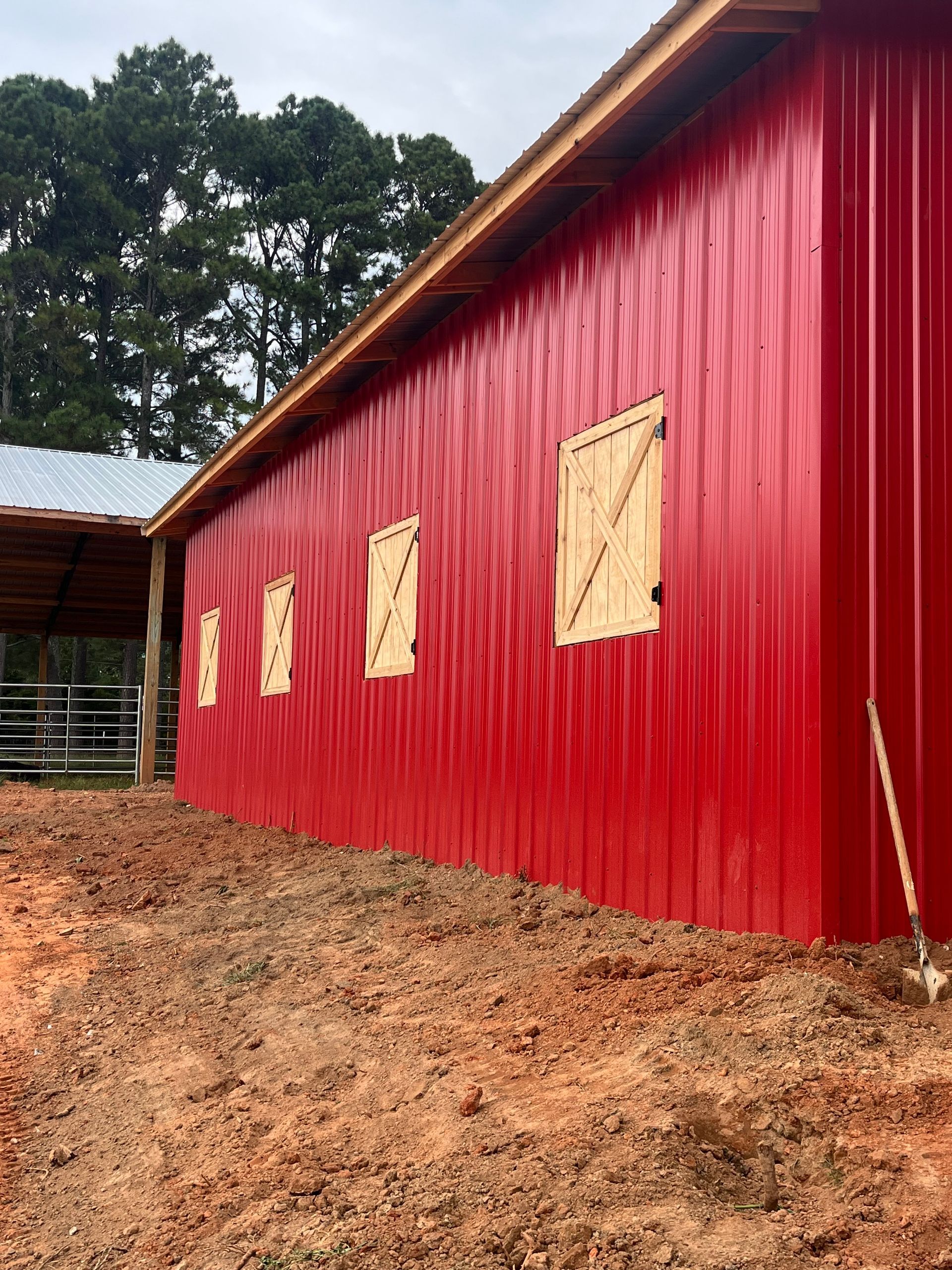 Red barn wall with boarded windows on a muddy dirt lot, trees in the background