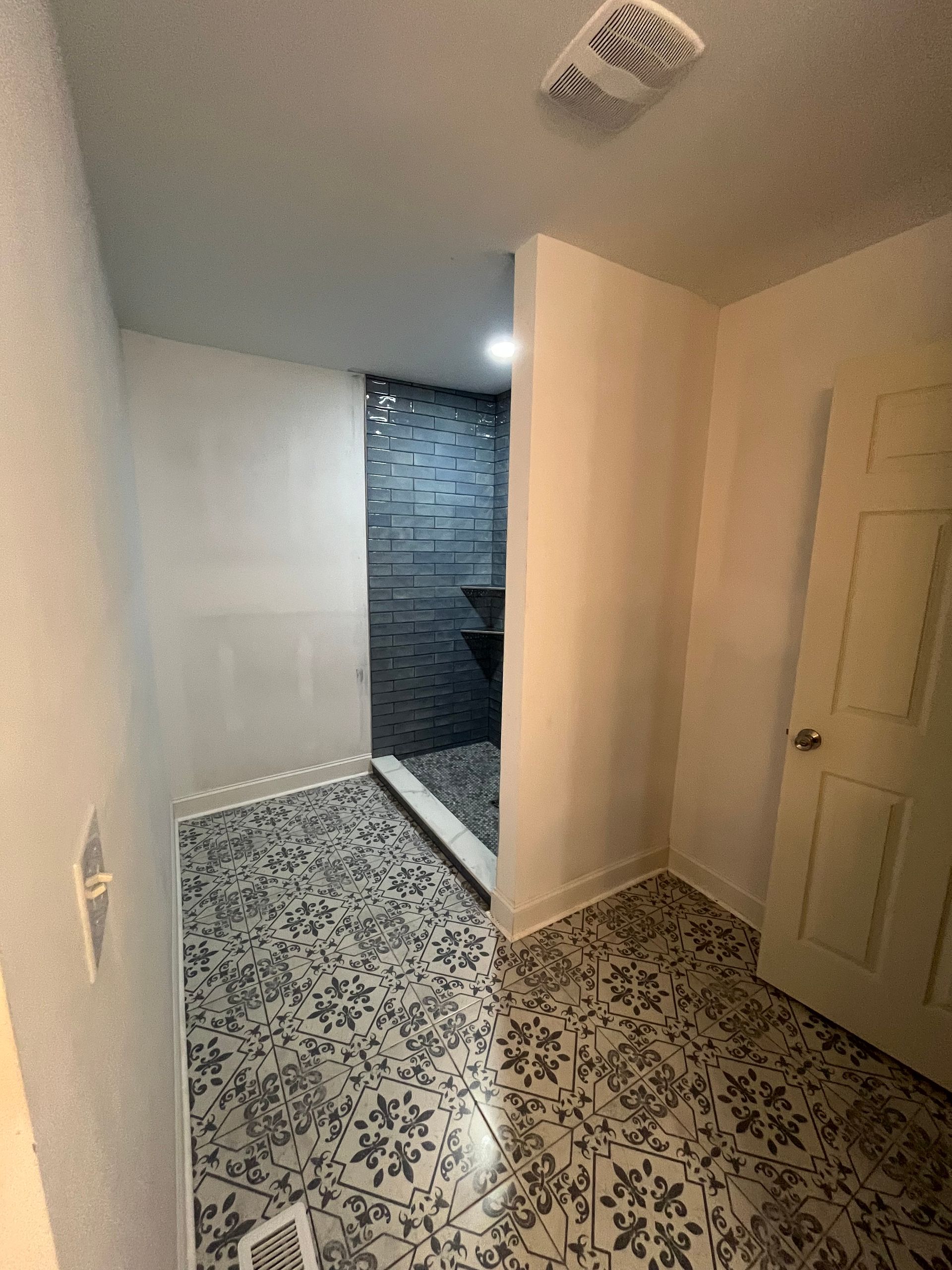 Narrow hallway with patterned tile floor, white walls, and a dark tiled doorway at the end.