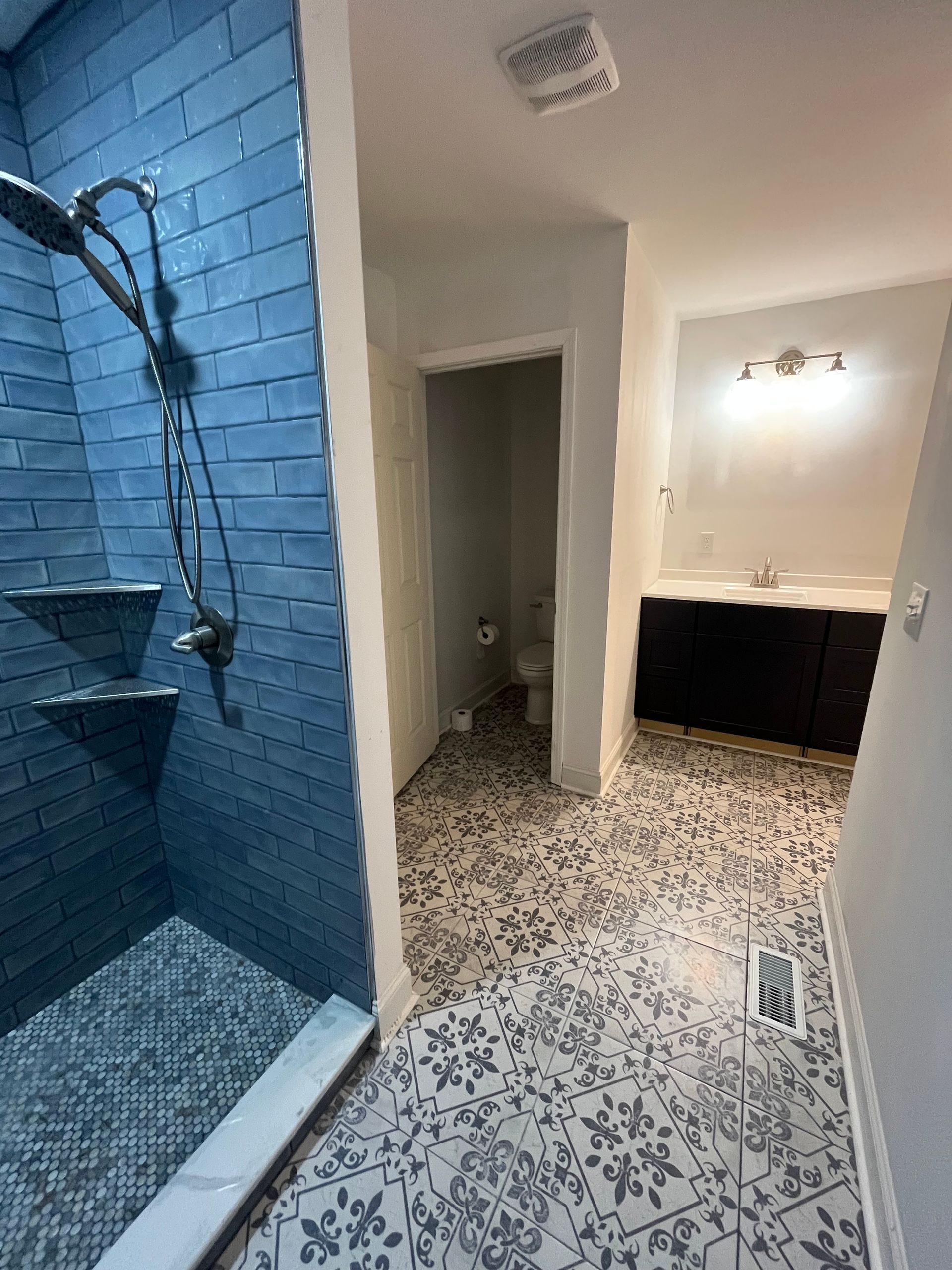 Blue-tiled shower beside a patterned bathroom floor leading to a vanity and mirror in a small bathroom.