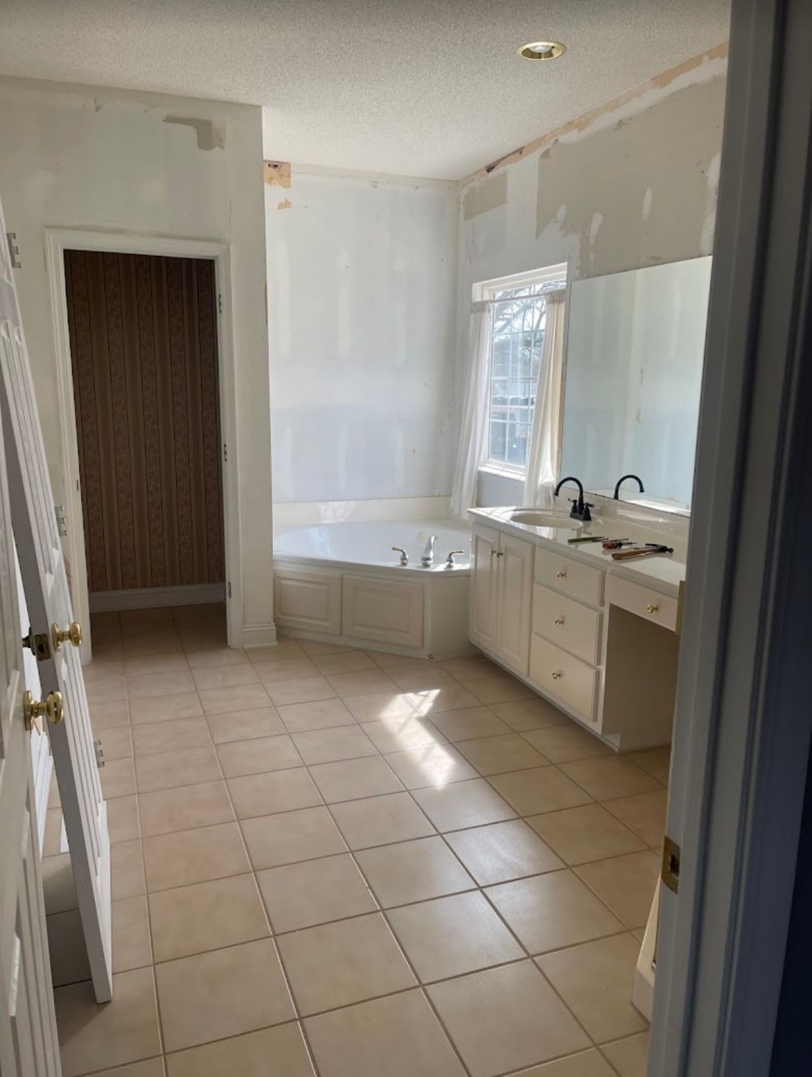 Empty kitchen with white cabinets, tiled floor, and sunlight streaming in through a window.