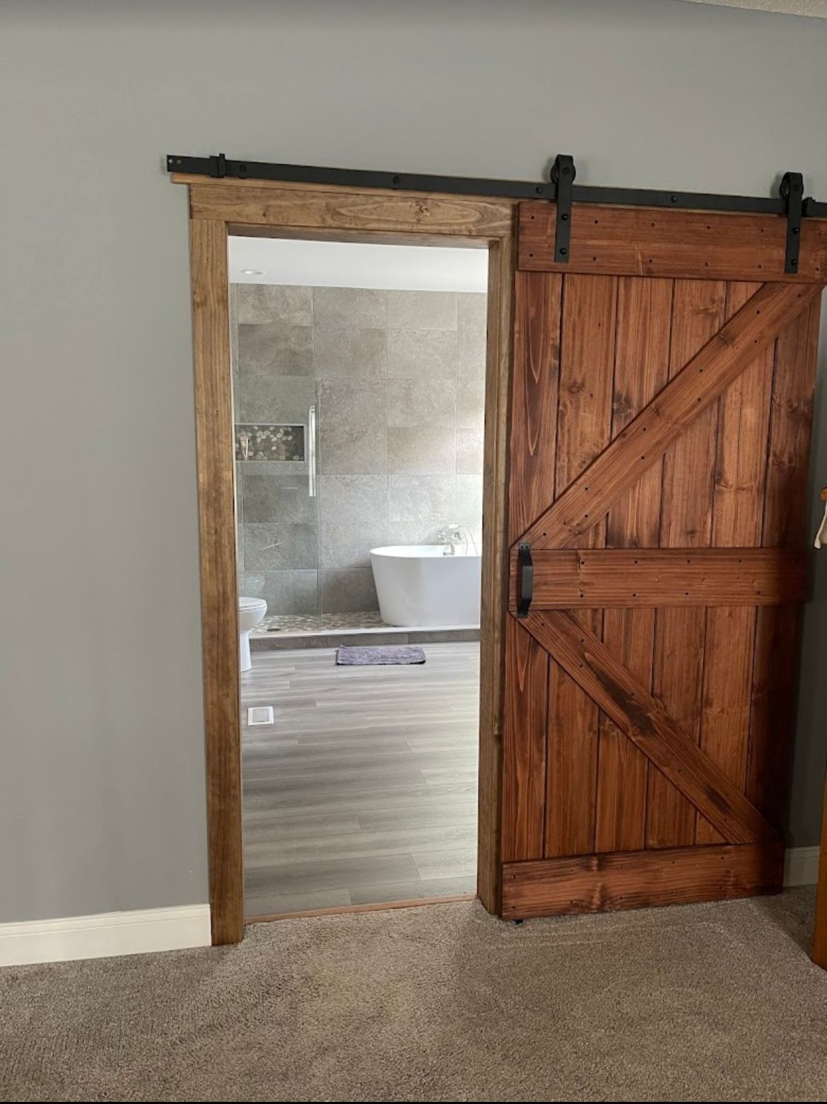 Rustic sliding barn door opens to a bathroom with a white tub and gray walls.
