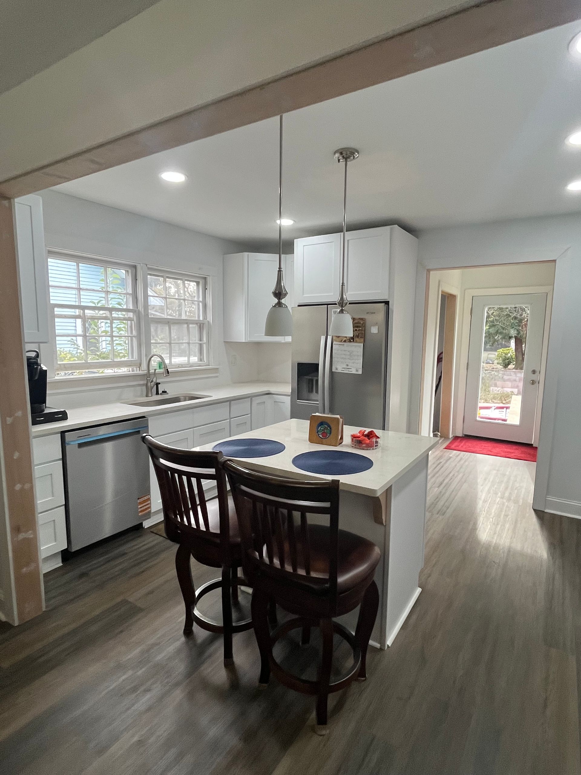 Modern kitchen with island, dark stools, white cabinets, stainless appliances, and a view of the backyard