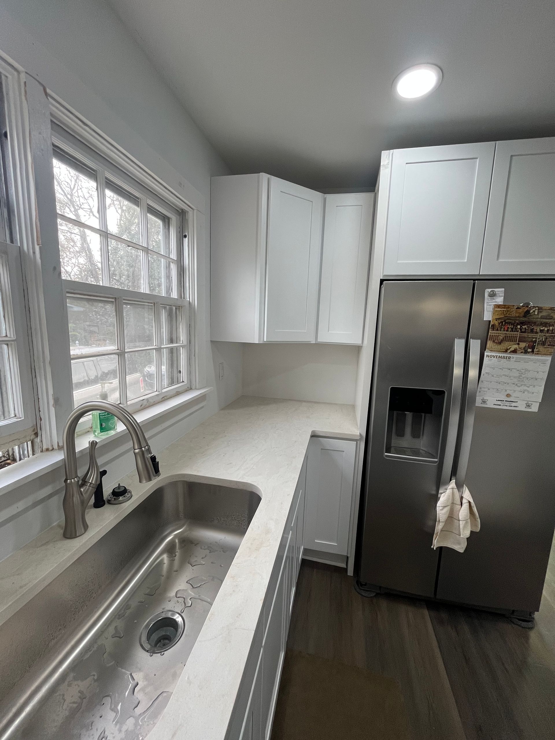 Bright modern kitchen with white cabinets, stainless sink, window, and refrigerator.