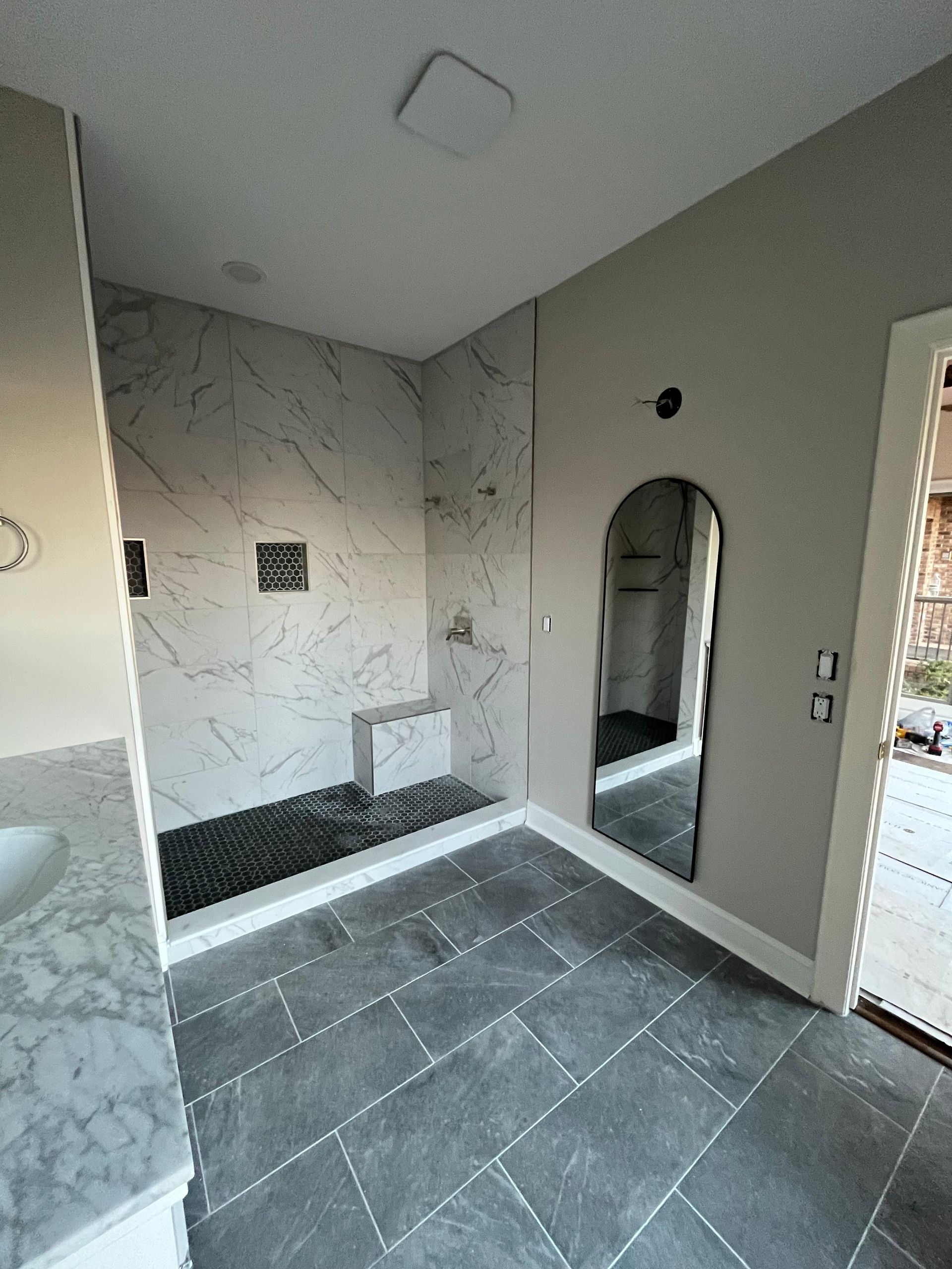Tiled shower room with gray marble-look walls, black bench, arched niche, and floor drain