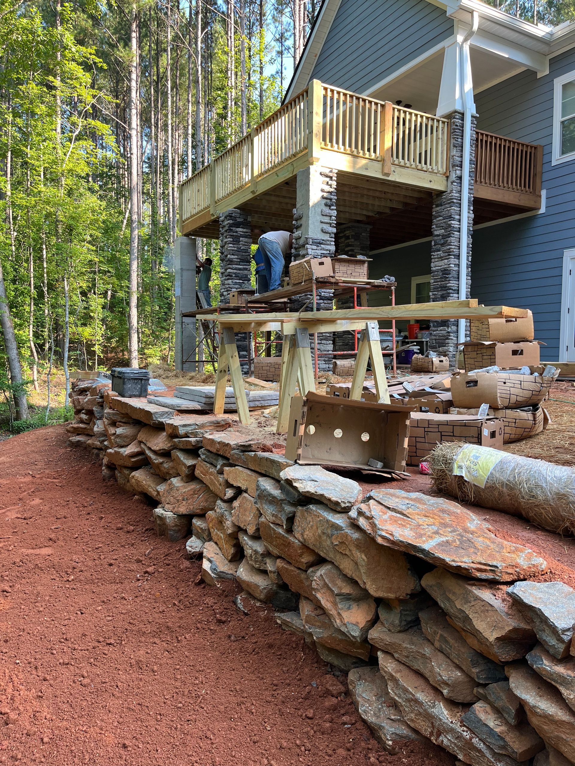 Raised wooden deck beside forest cabin with stacked stone wall and red gravel path