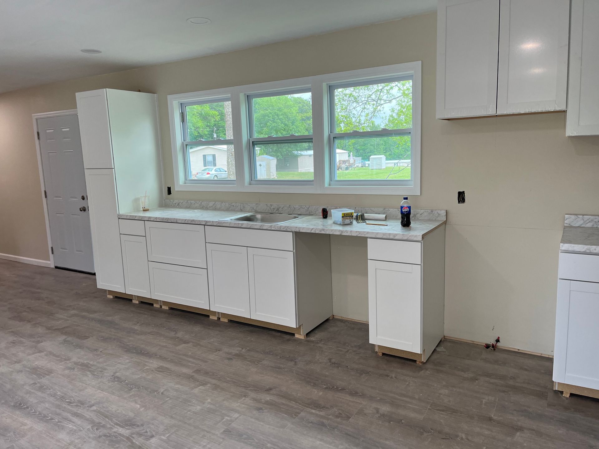 Unfinished kitchen with white cabinets, a large window, and a wood-look floor.