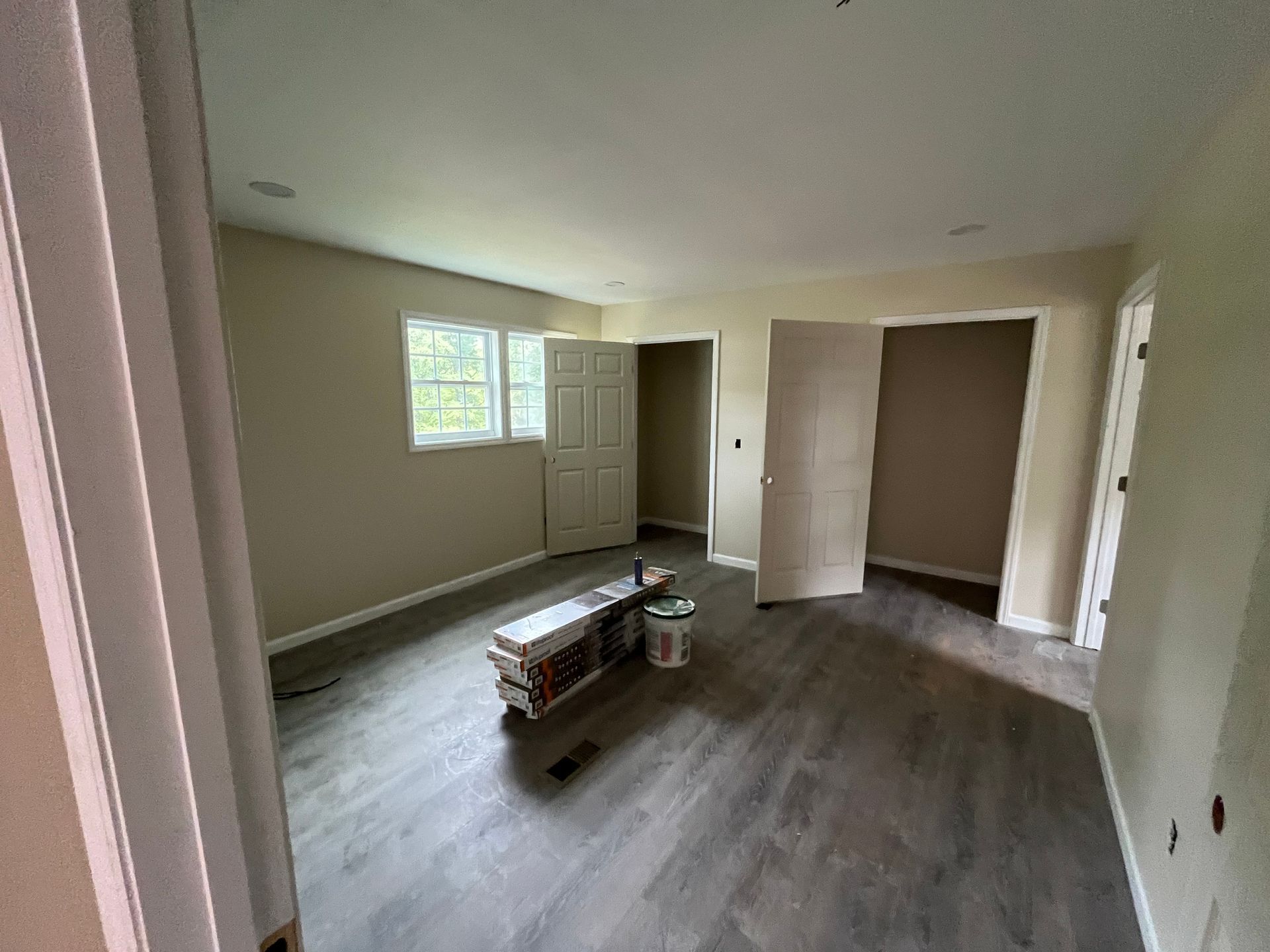 Empty room with gray wood flooring, two windows, and a box on the floor under renovation