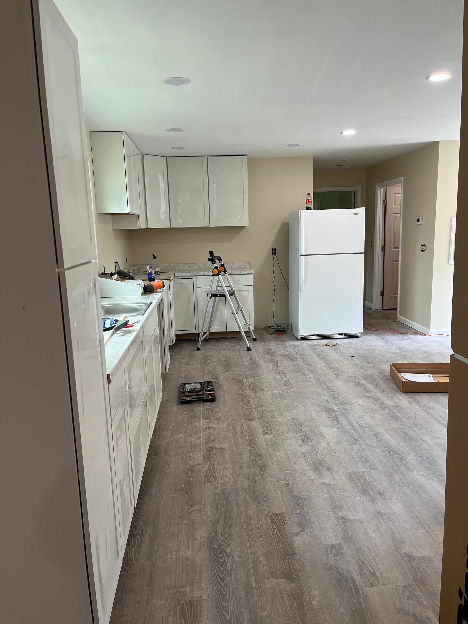 Empty kitchen and living area with white cabinets, refrigerator, and wood-look flooring