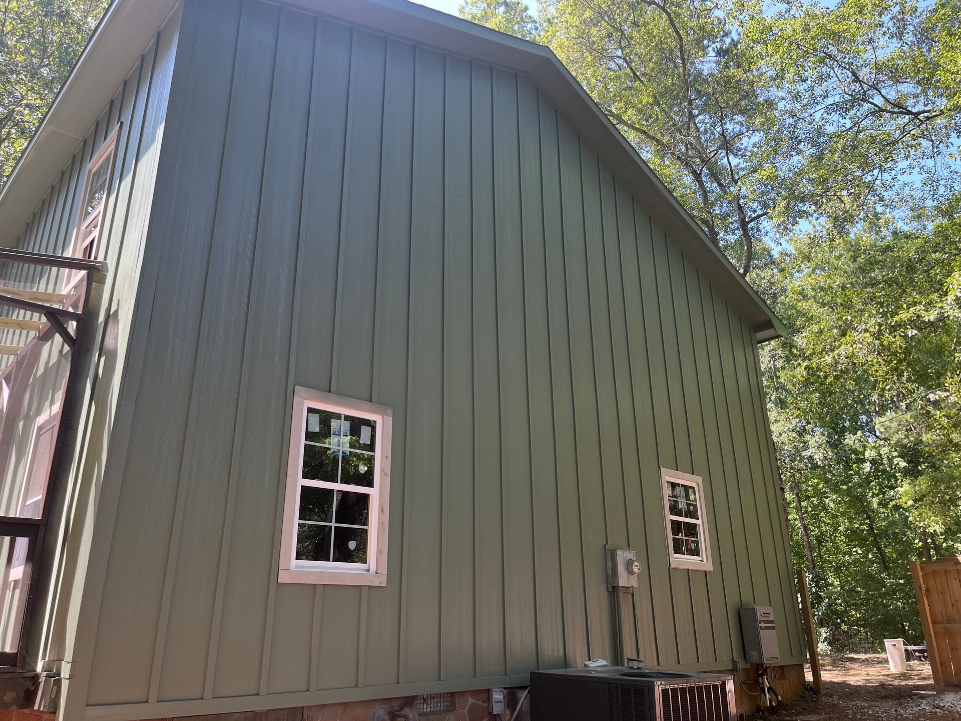 Green barn-style building with white-trimmed windows under trees and a blue sky